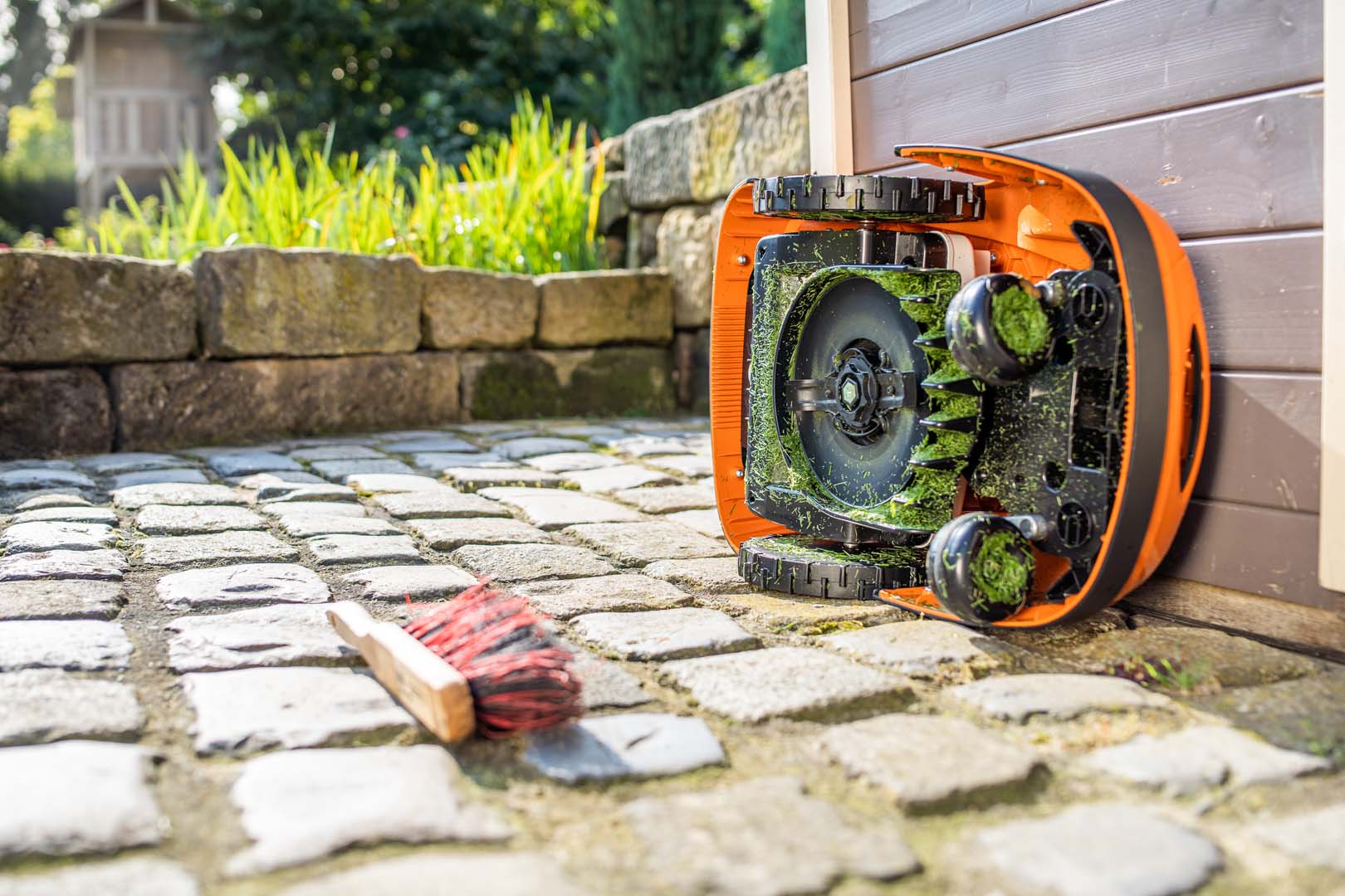 STIHL iMOW® -robottiruohonleikkuri käännettynä kyljelleen valmiina puhdistettavaksi, harja maassa lähellä