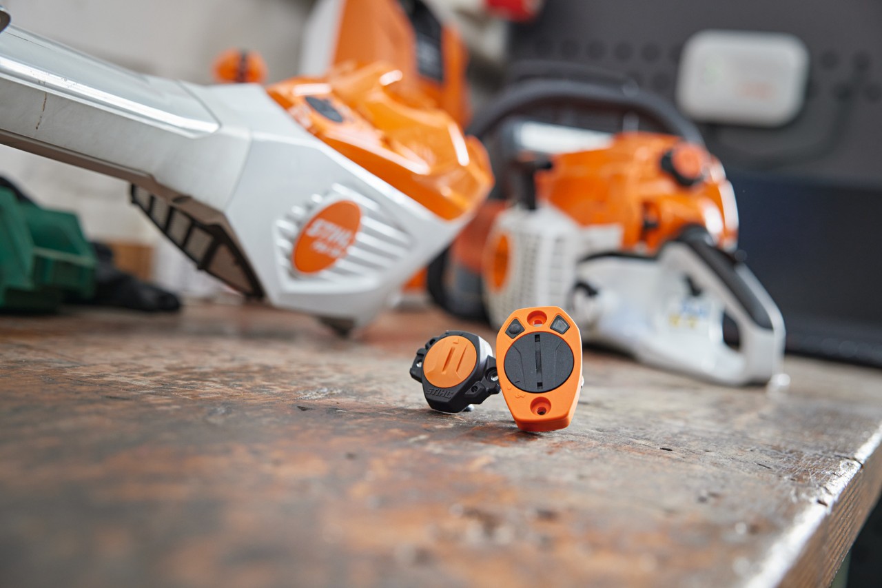 STIHL Smart Connector ja STIHL Smart Connector 2 A työpöydällä. Taustalla näkyy erilaisia STIHL-työkaluja epätarkasti.