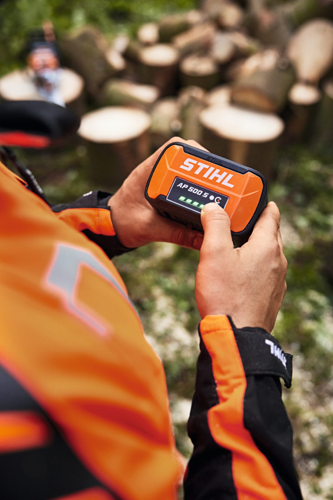 Henkilö pitämässä STIHL AP 500 S -akkua käsissään. Vihreä valo varaustason näytön LED-merkkivaloissa. 