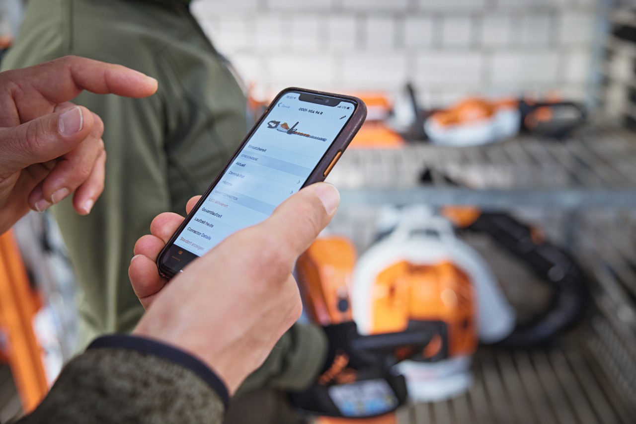 Varastossa oleva henkilö tarkistaa päivämäärän STIHL connected -sovelluksessa älypuhelimella.