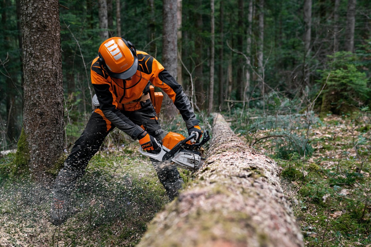 Suojavarusteita käyttävä mies sahaamassa kaadettuja puunrunkoja bensiinikäyttöisellä STIHL MS 400 C-M -moottorisahalla, jossa on magnesiummäntä