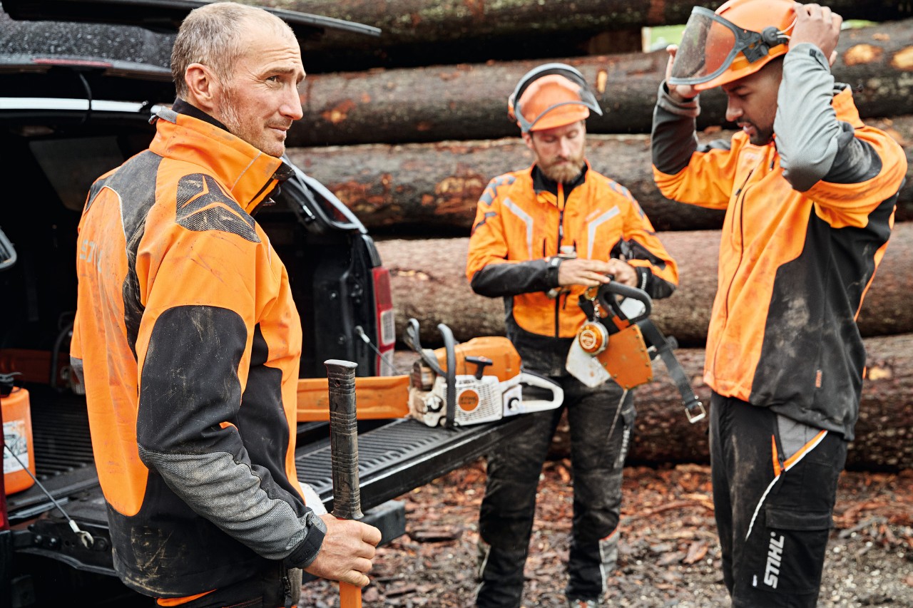 Kolme STIHL-suojavarusteita käyttävää miestä ajoneuvon vieressä tavaratila avoinna
