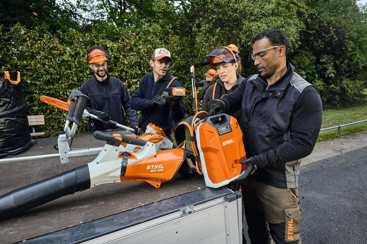 Kolme miestä ja yksi nainen STIHL-suojavarusteissa seisoo ajoneuvon lavalla STIHL-koneiden, kuten akkukäyttöisen STIHL BGA 200 -lehtipuhaltimen ja STIHL AR 2000 L -reppuakun kanssa 