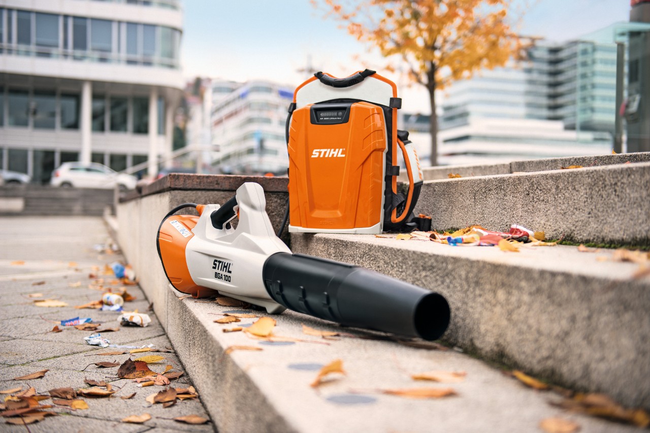Akkukäyttöinen STIHL BGA 100 -lehtipuhallin ja ammattikäyttöön tarkoitettu STIHL AR 3000 L -reppuakku kiviporraskäytävällä, jossa on muutama lehti