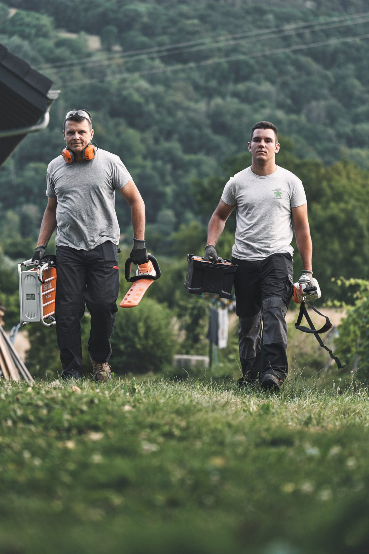 Kaksi ammattilaista kävelemässä STIHL-akkutyökalujen kanssa pellon läpi