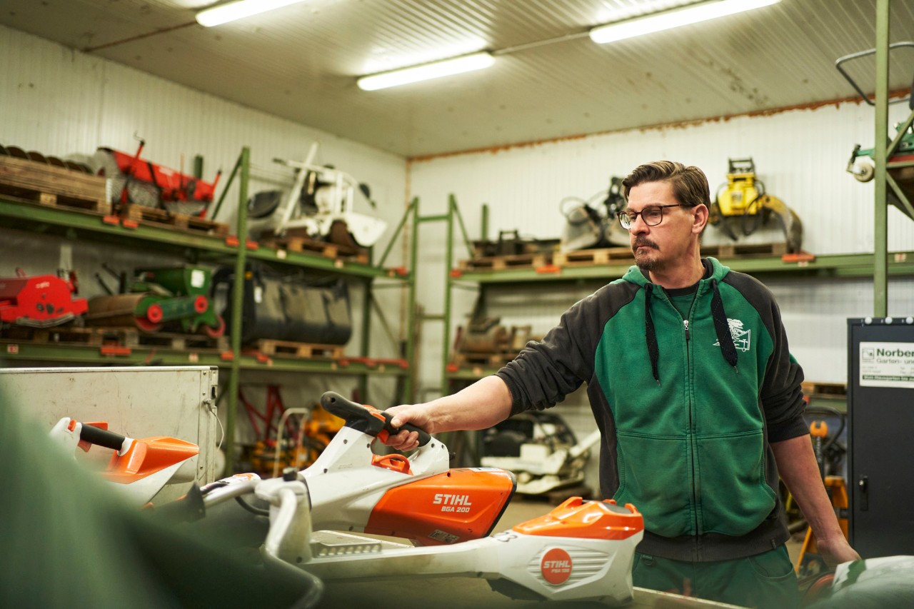 Mies seisomassa korjaamossa STIHL akkutyökalujen takana kurottamassa akkukäyttöiseen STIHL BGA 200 -lehtipuhaltimeen