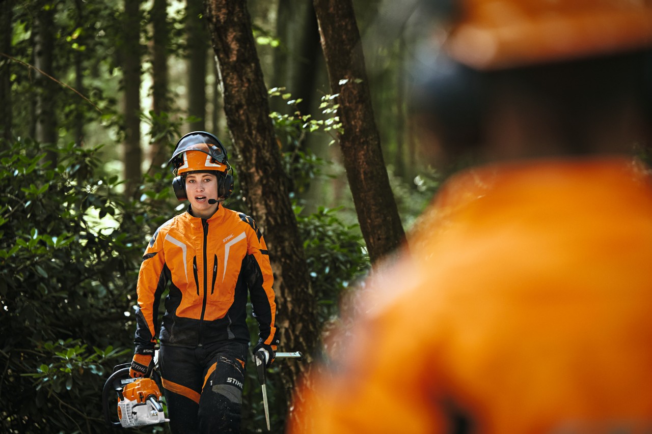 En man och en kvinna med STIHL sladdlösa motorsågar och en STIHL sladdlös beskärare går leende mot en bil 