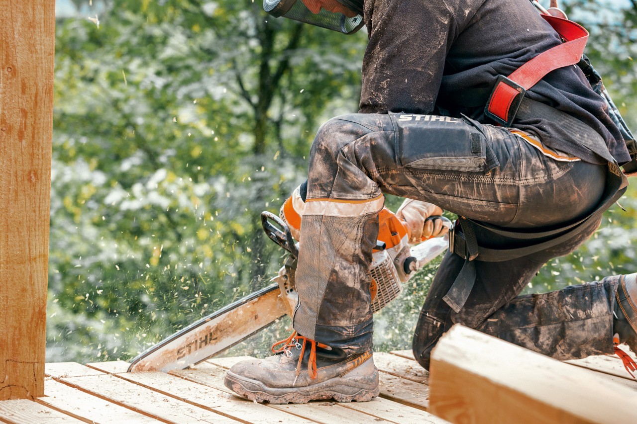 Työsaappaita ja STIHL Advance X-Light -housuja käyttävä henkilö sahaamassa puutasanteen reunaa STIHL-moottorisahalla