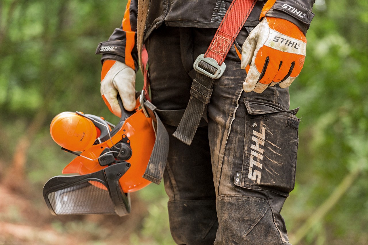 STIHL-työhousuja ja -käsineitä sekä suojakypärää käyttävä henkilö 