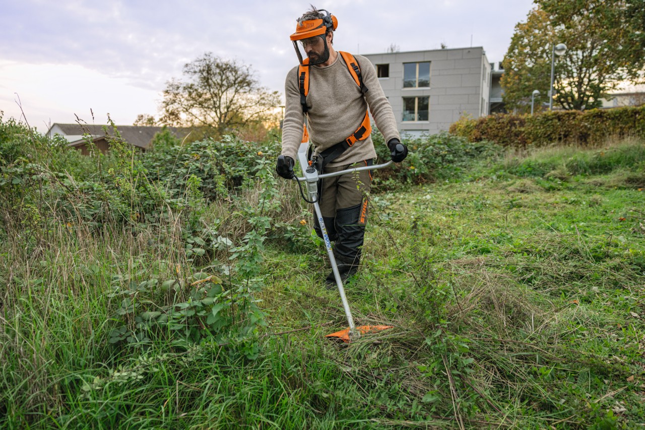 STIHL suojavarusteita käyttävä mies leikkaamassa villiä ja viljeltyä viheraluetta akkukäyttöisellä STIHL FSA 200 -raivaussahalla