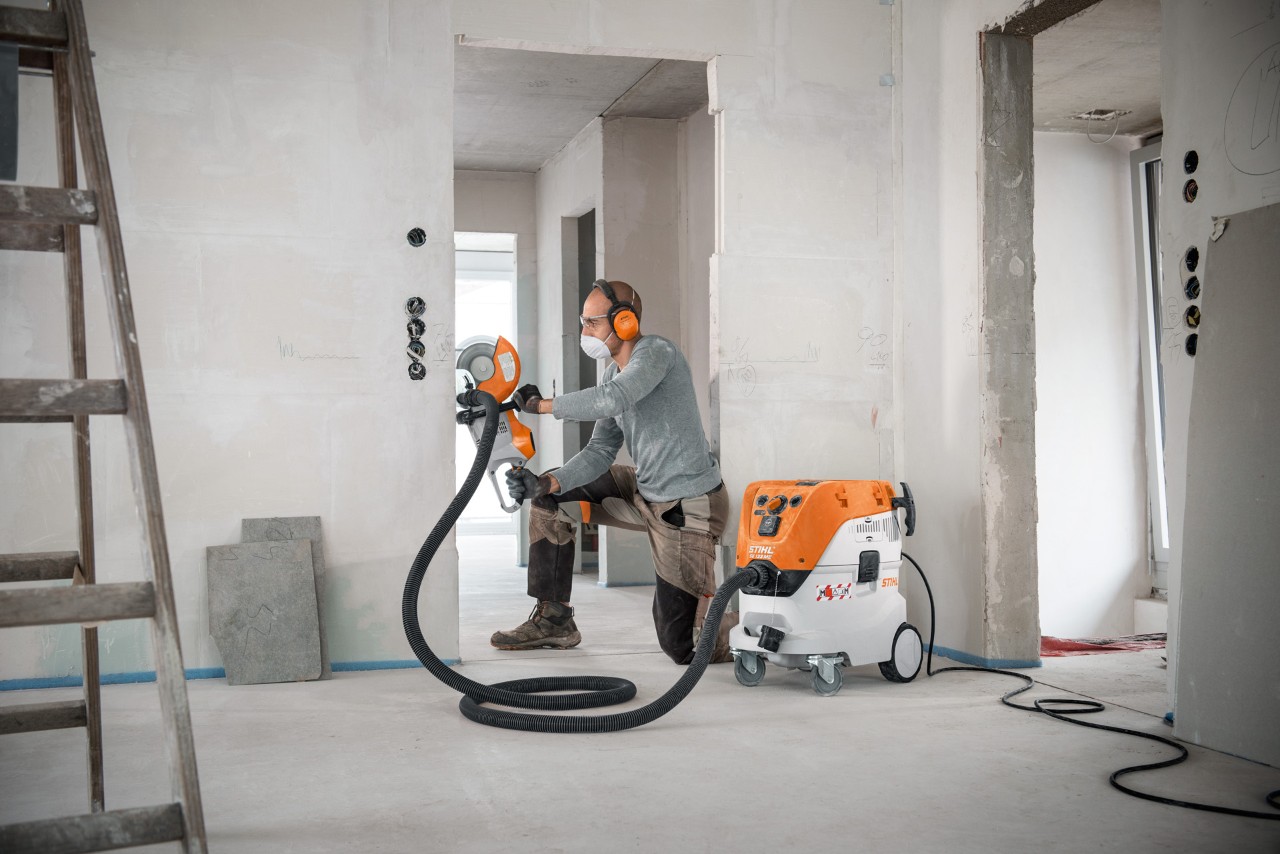 STIHL SE 133 ME -märkä-kuivaimuria käyttävä mies työskennellessään STIHL TSA 230 -laikkaleikkurilla