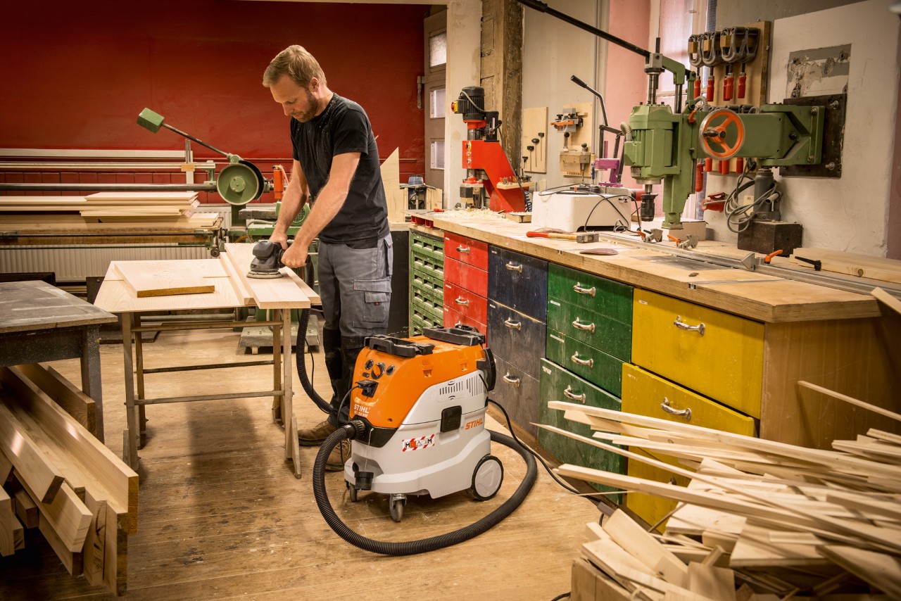 Mies käyttämässä STIHL SE 133 ME -märkä-kuivaimuria työpajassa työskennellessään puulankkujen parissa