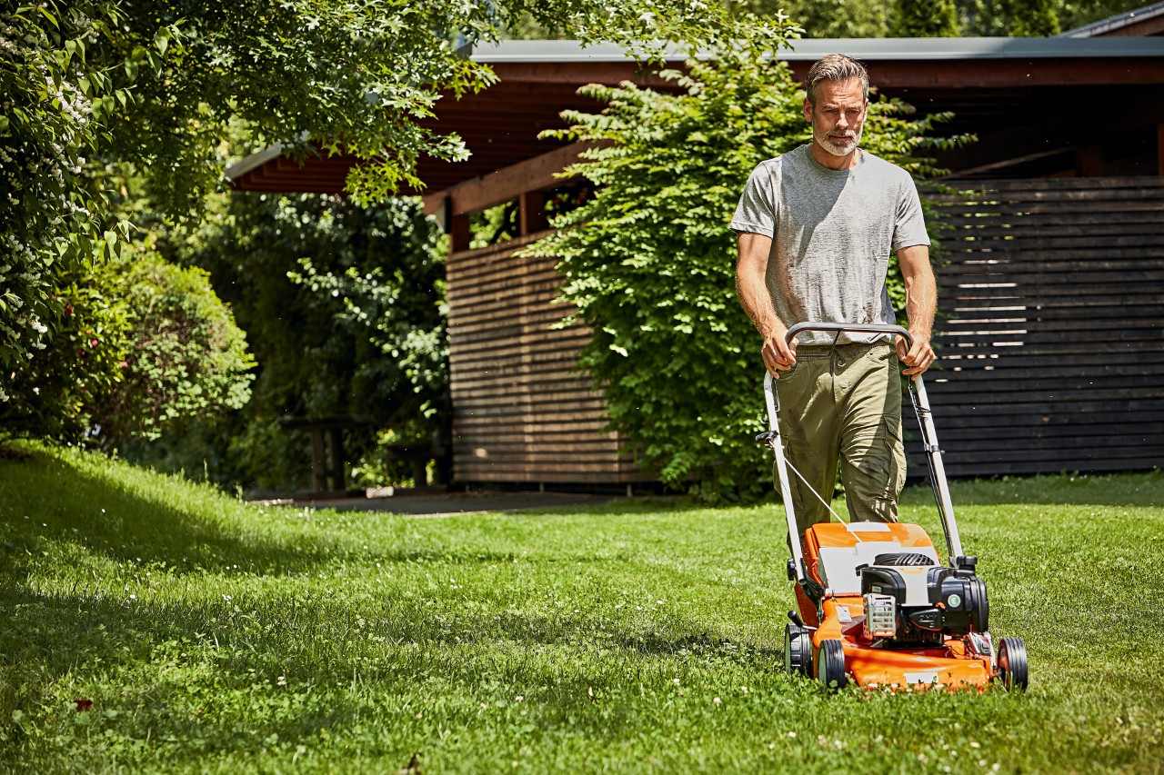  Mies leikkaa nurmikkoa polttomoottorikäyttöisellä STIHL-ruohonleikkurilla RM 248 puutarhavajan edessä