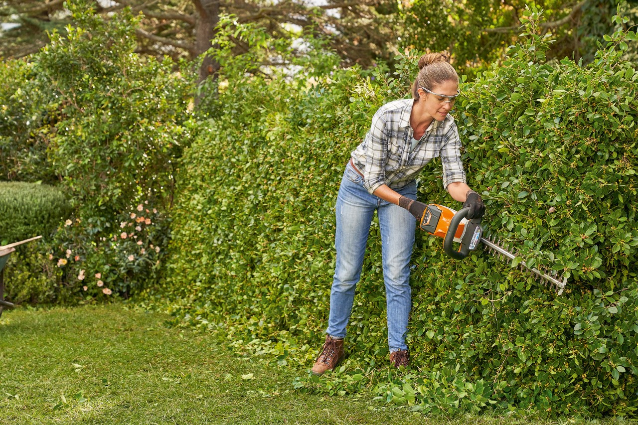 Nainen leikkaa pensasaitaa STIHL HS 82 pensasleikkurilla