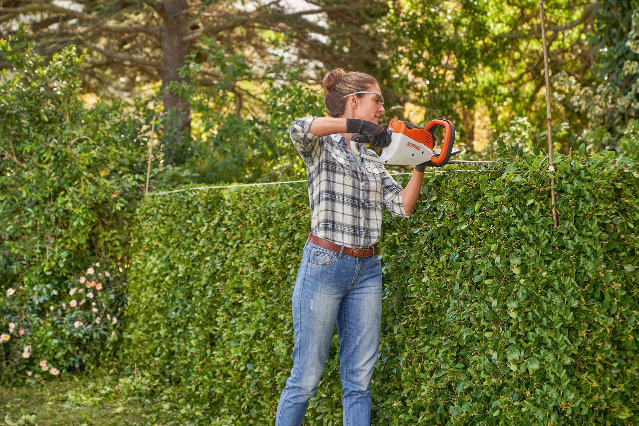 Nainen leikkaa pensasaidan muotoonsa STIHL HSA 45 -akkupensasleikkurilla