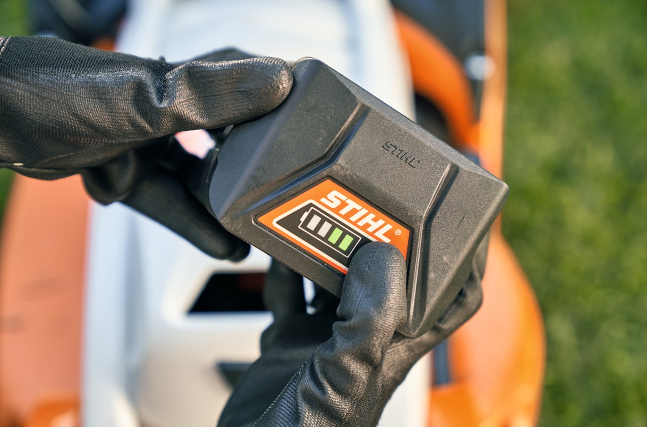 STIHL-litiumioniakku, taustalla akkukäyttöinen STIHL RMA 339 C -ruohonleikkuri