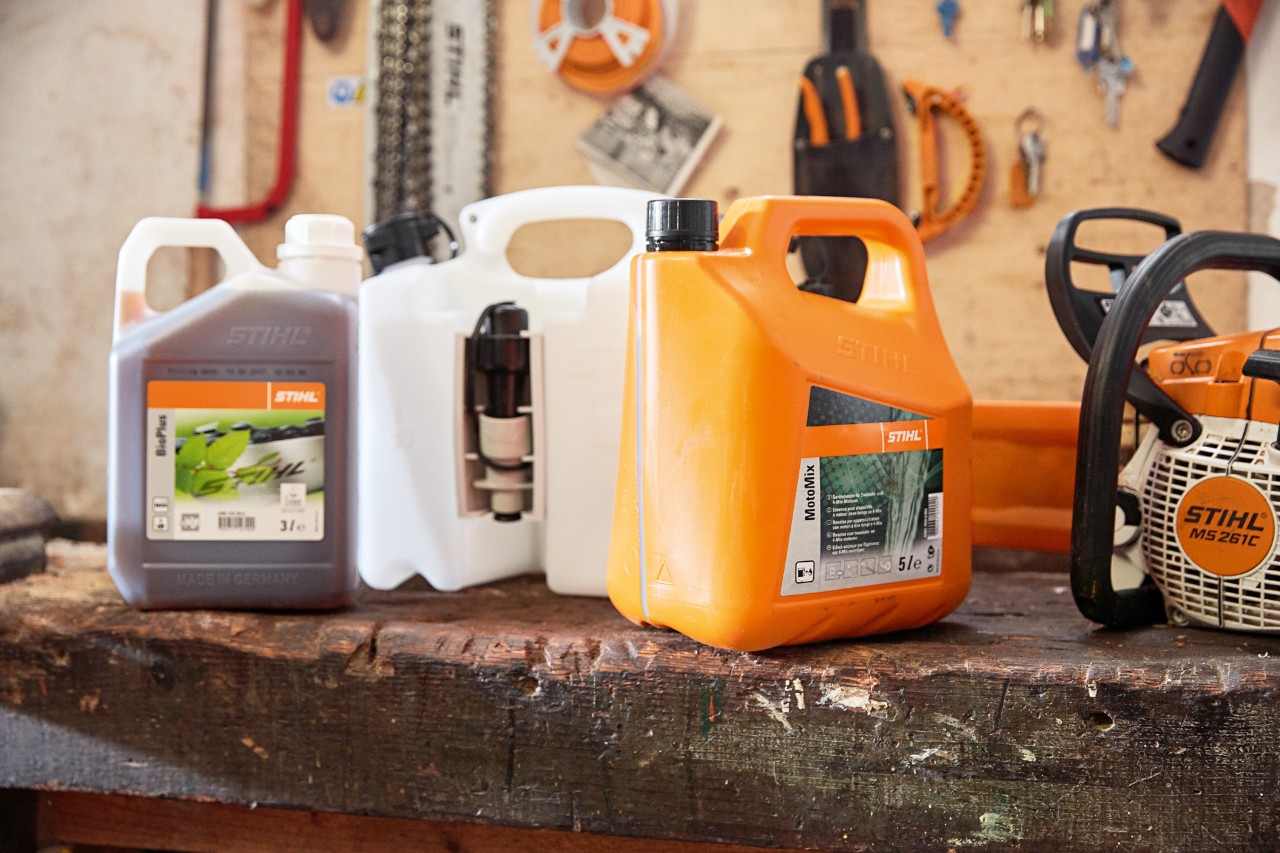 Säiliö, jossa on STIHL MotoMix -moottorisahaseosta, öljyä ja bensiiniä, sekä bensiinikäyttöinen STIHL MS 261 C -moottorisaha korjaamolla