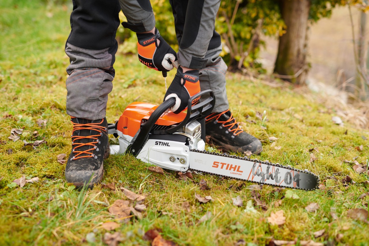Käsineitä käyttävä henkilö käynnistämässä bensiinikäyttöistä STIHL MS 261 C-M -moottorisahaa, jossa on Light 04 -terälaippa