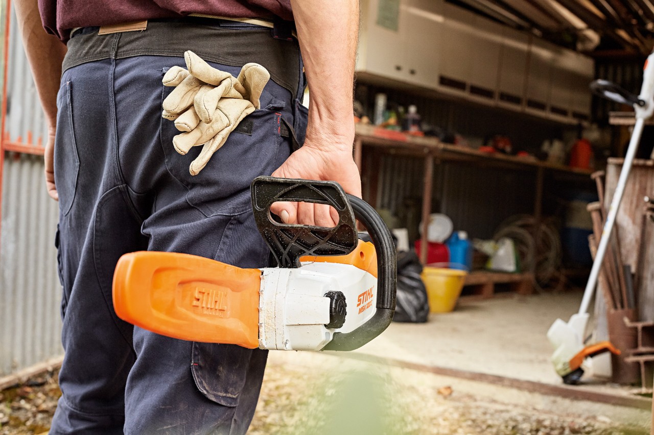 Mies kävelemässä työpajaan kuljettaen akkukäyttöistä STIHL-moottorisahaa, jossa on suojalevy