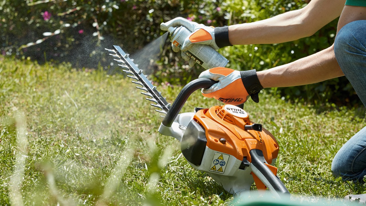 Bensiinikäyttöistä STIHL HS 82 T -pensasleikkuria puhdistetaan nurmikolla
