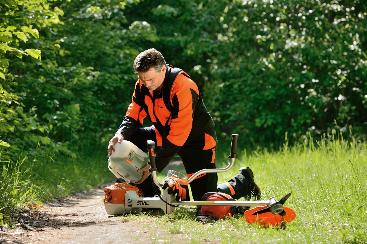 Mies lisäämässä bensiinin ja öljyn seosta STIHL-raivaussahaan