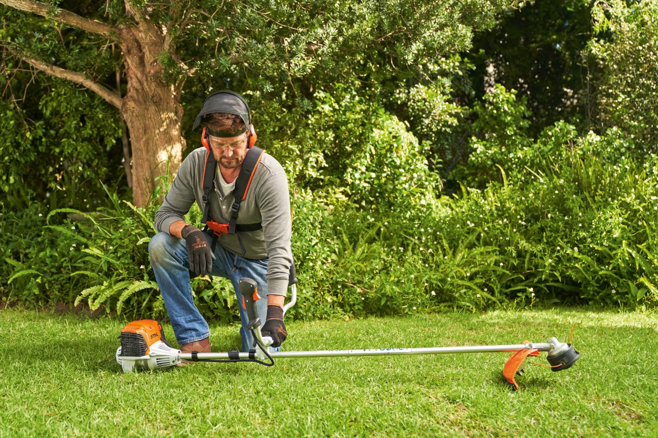 Mies asettamassa bensiinikäyttöistä STIHL FS 91 -moottorisahaa maahan sen käynnistämiseksi