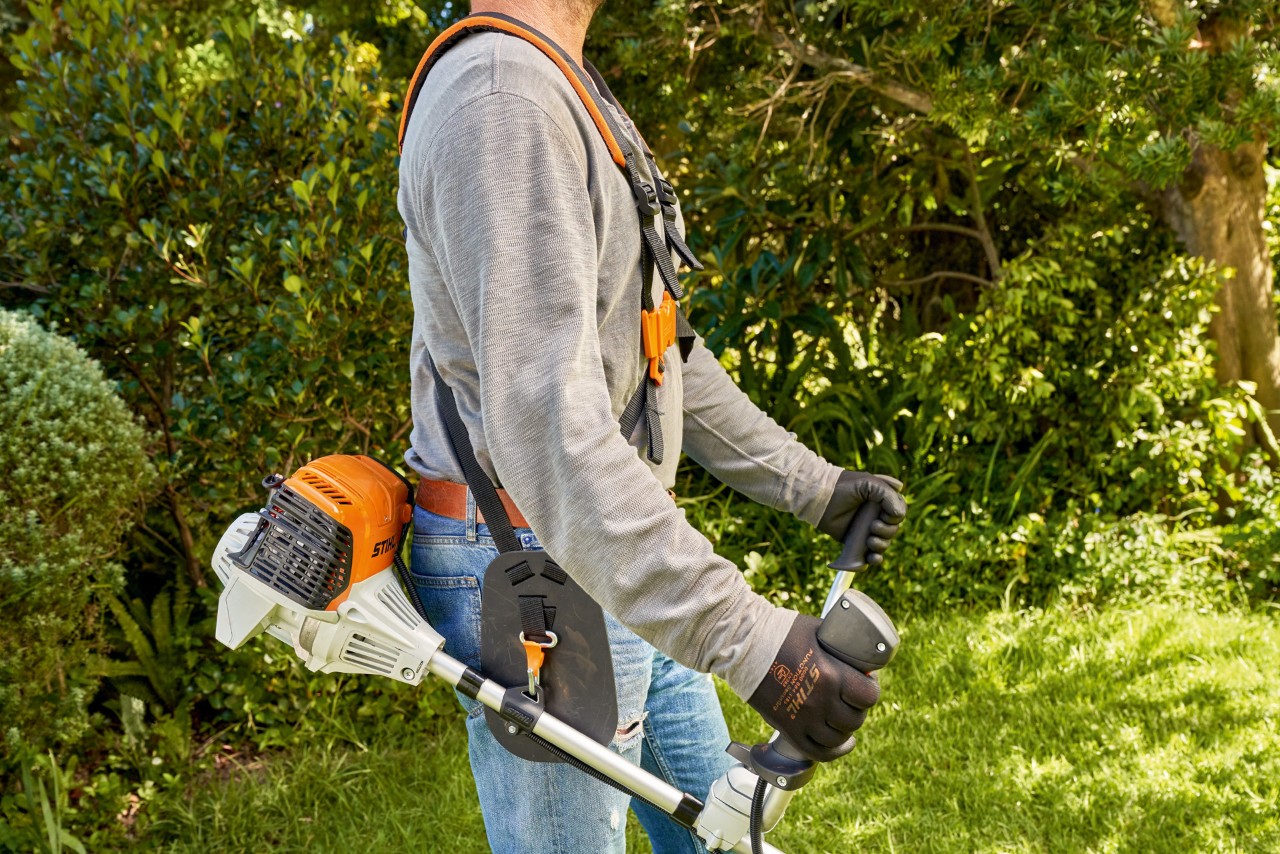 Mies nostamassa bensiinikäyttöistä STIHL FS 91 -raivaussahaa maasta ruohonleikkuun aloittamiseksi 
