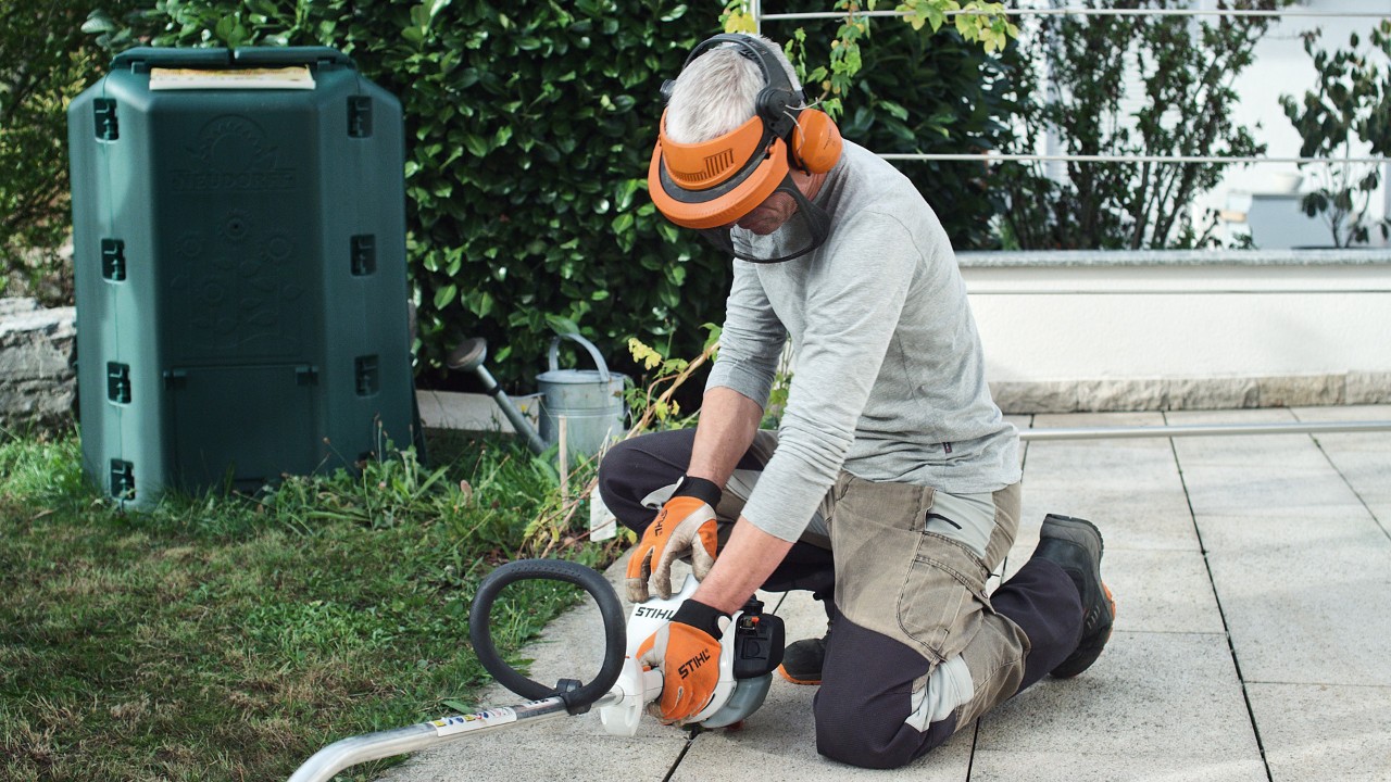 Suojavaatteita käyttävä henkilö painamassa bensiinikäyttöistä STIHL FS 38 -raivaussahaa maahan