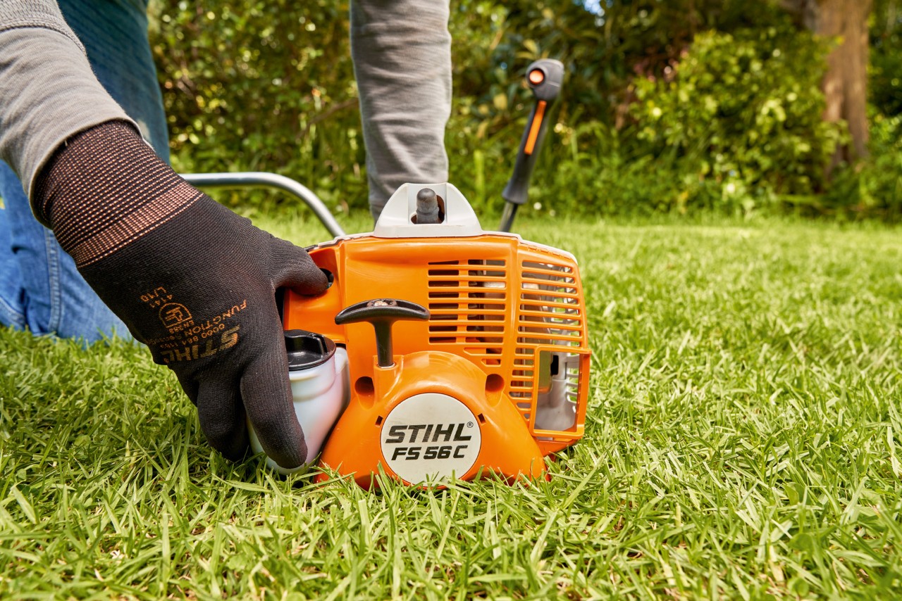 Mies käynnistämässä bensiinikäyttöistä STIHL FS 56 -raivaussahaa painamalla polttoainepumppua
