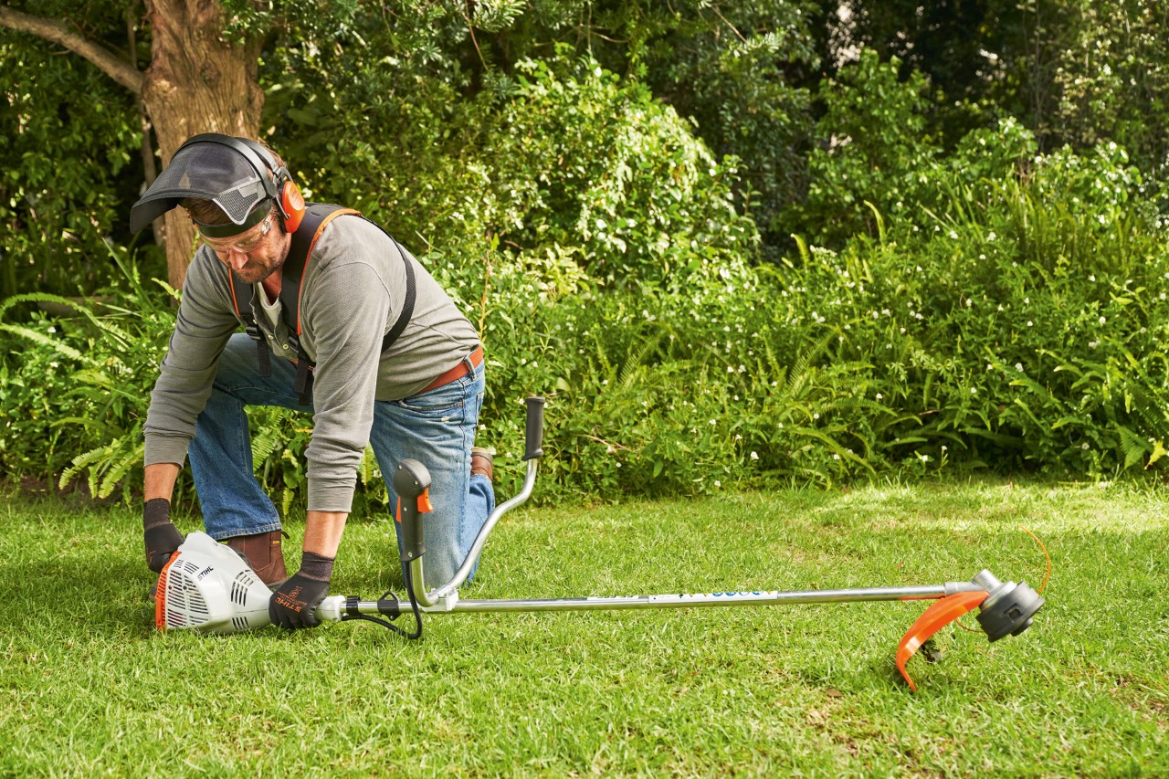 Mies painamassa bensiinikäyttöistä STIHL FS 56 -moottorisahaa maahan sen käynnistämiseksi