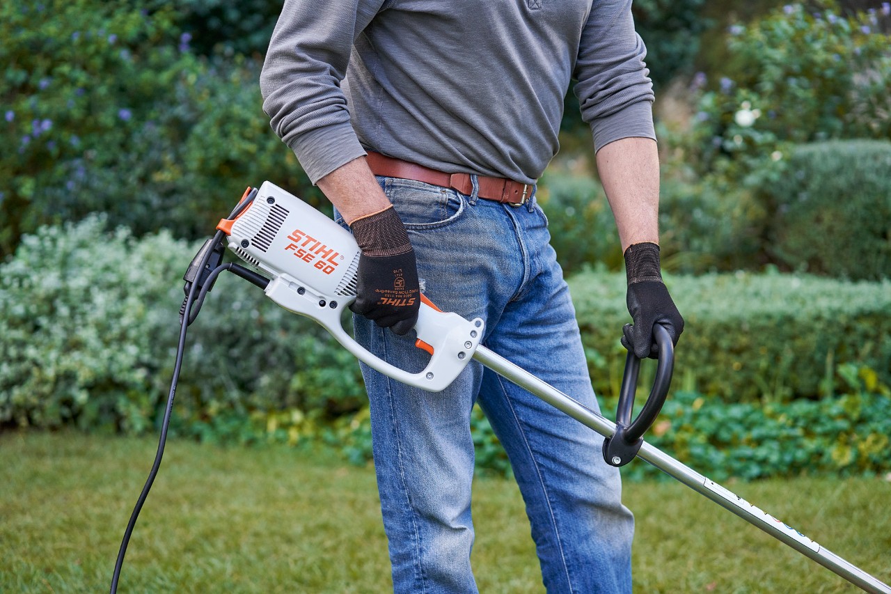Suojakäsineitä käyttävä mies pitelemässä sähkökäyttöistä STIHL FSE 60 -raivaussahaa molemmin käsin