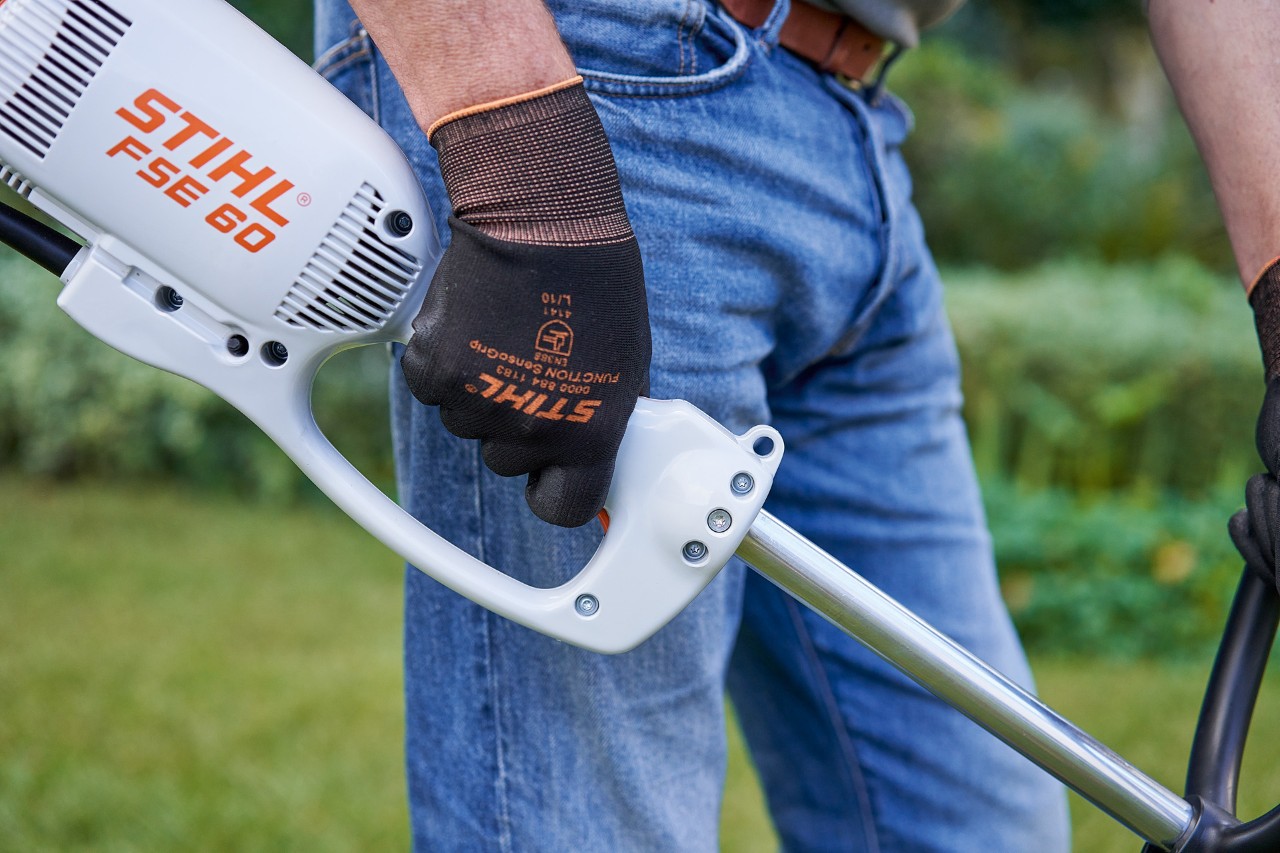 Mies painamassa sähkökäyttöisen STIHL FSE 60 -raivaussahan ohjauskahvan kytkintä