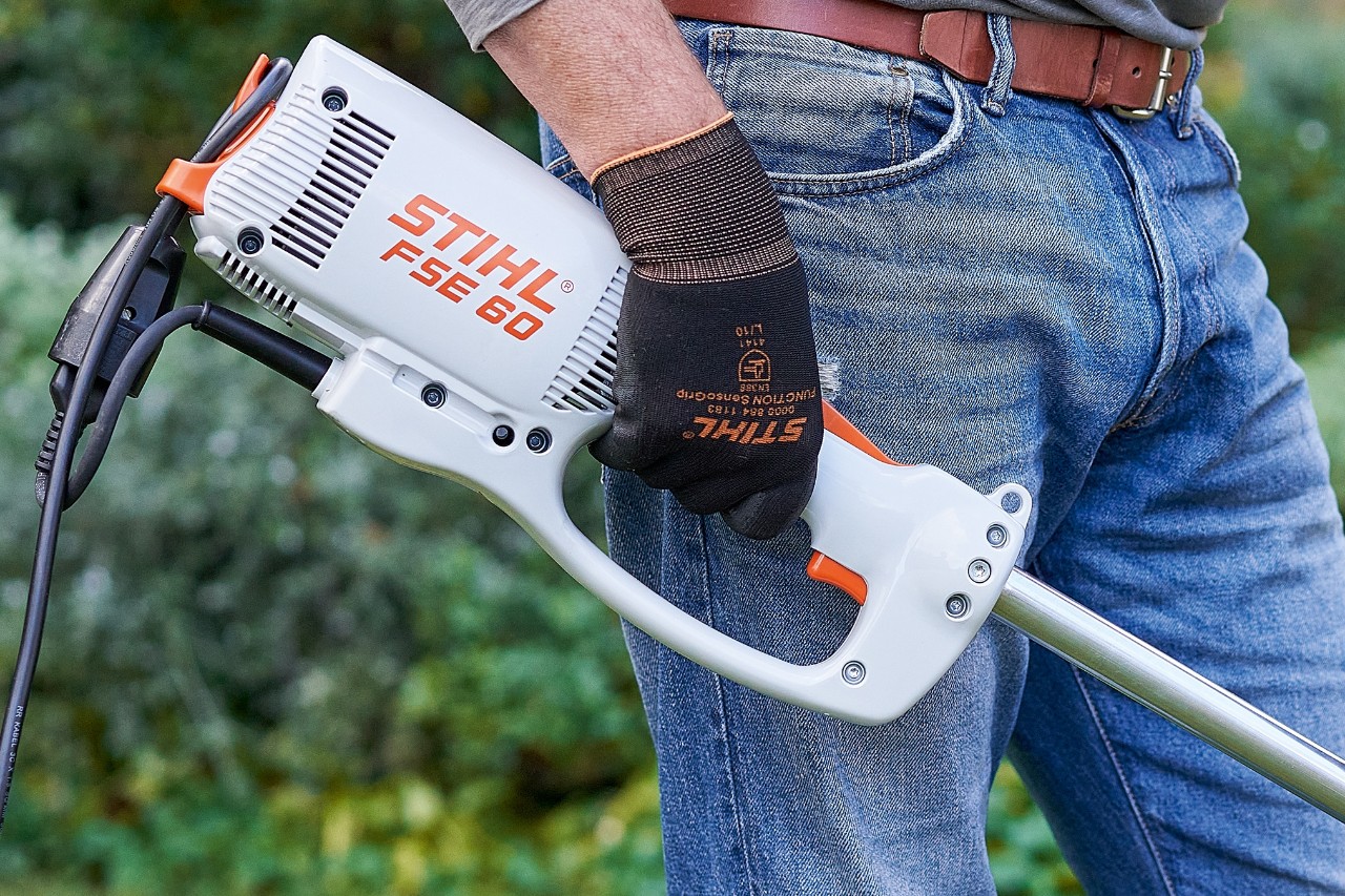 Mies painamassa sähkökäyttöisen STIHL FSE 60 -raivaussahan kytkintä sahan sammuttamiseksi.