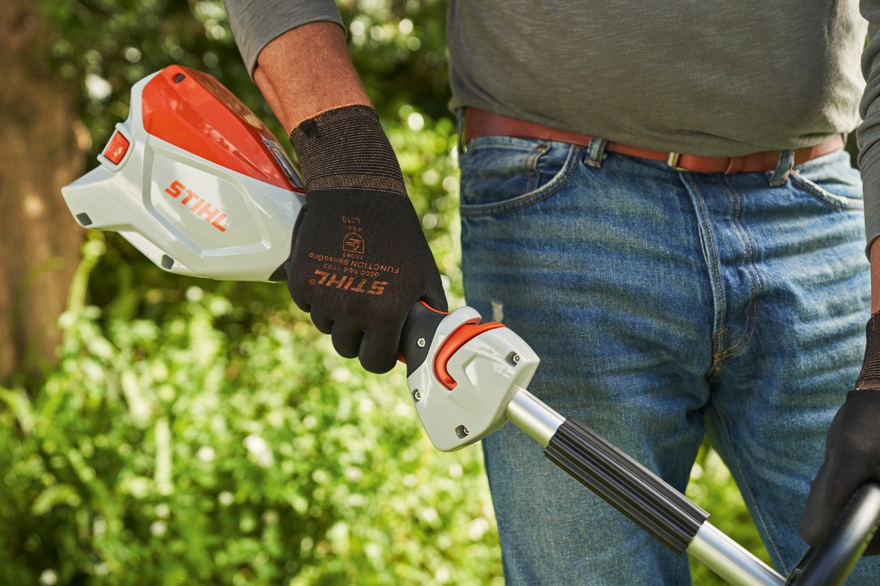 Suojakäsineitä käyttävä mies käynnistämässä akkukäyttöistä STIHL FSA 60 -raivaussahaa painamalla liipaisinta