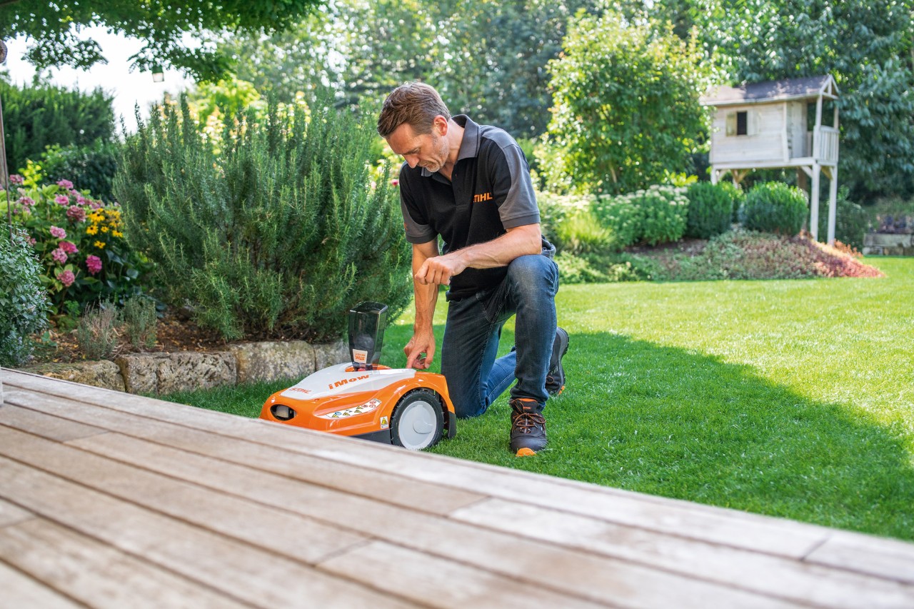 STIHL-jälleenmyyjä käyttämässä STIHL iMOW® 422 -robottiruohonleikkurin ohjauspaneelia puutarhassa