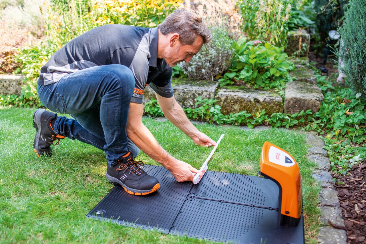 STIHL-jälleenmyyjä asentamassa STIHL iMOW® 422 -robottiruohonleikkuria telakointiasemaan puutarhassa