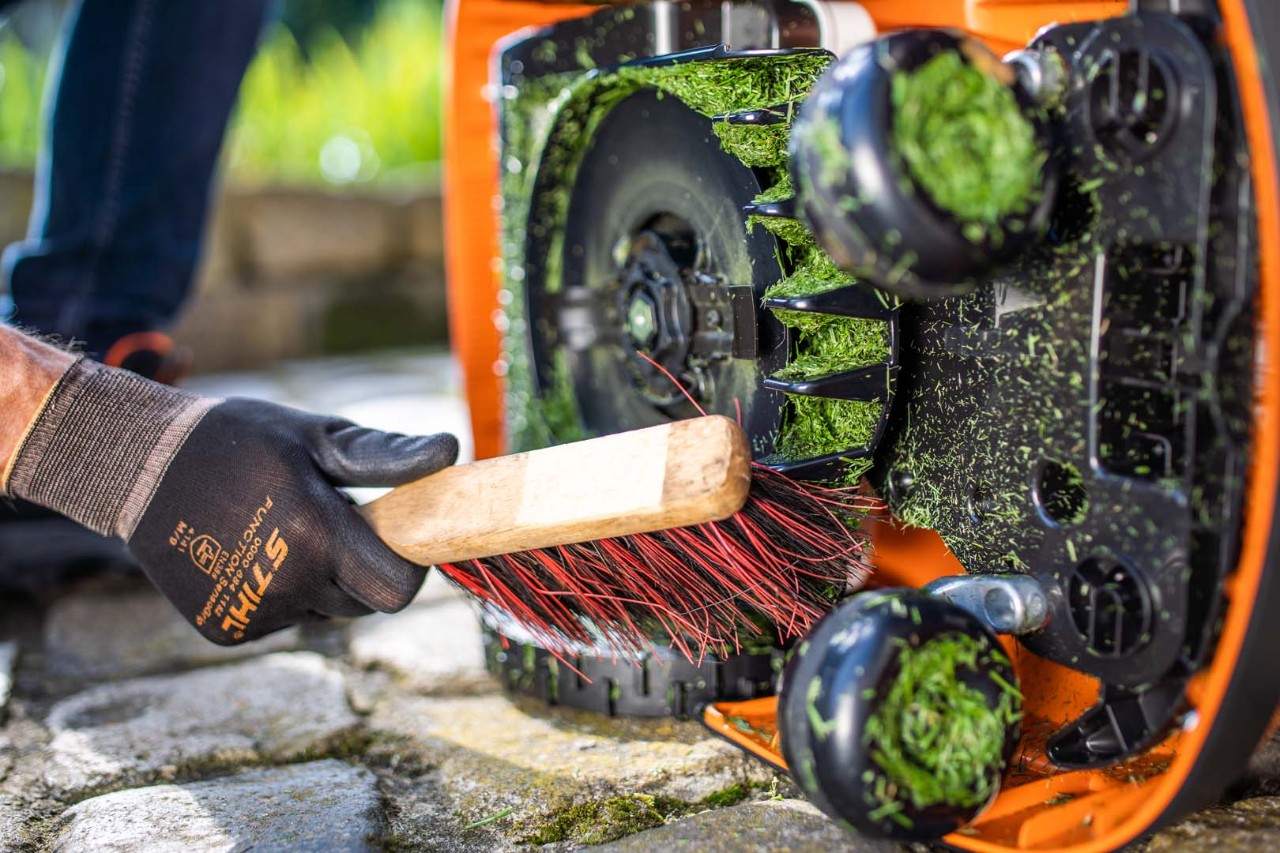 STIHL iMOW® -robottiruohonleikkurin leikkuulaitteen puhdistus harjalla sivulta käsineitä käyttäen
