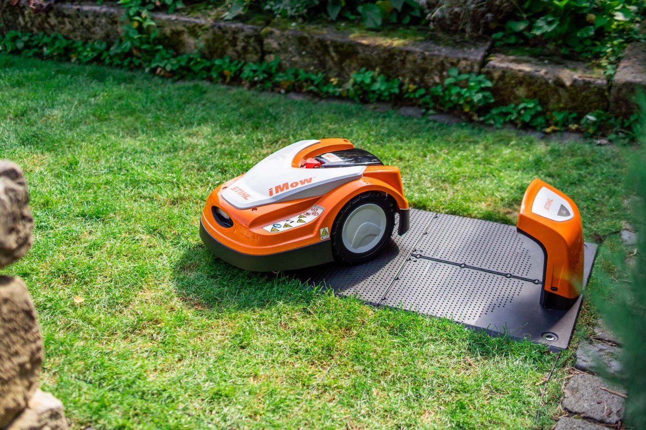 STIHL iMOW® -robottiruohonleikkuri telakointiaseman vieressä vihreällä nurmikolla