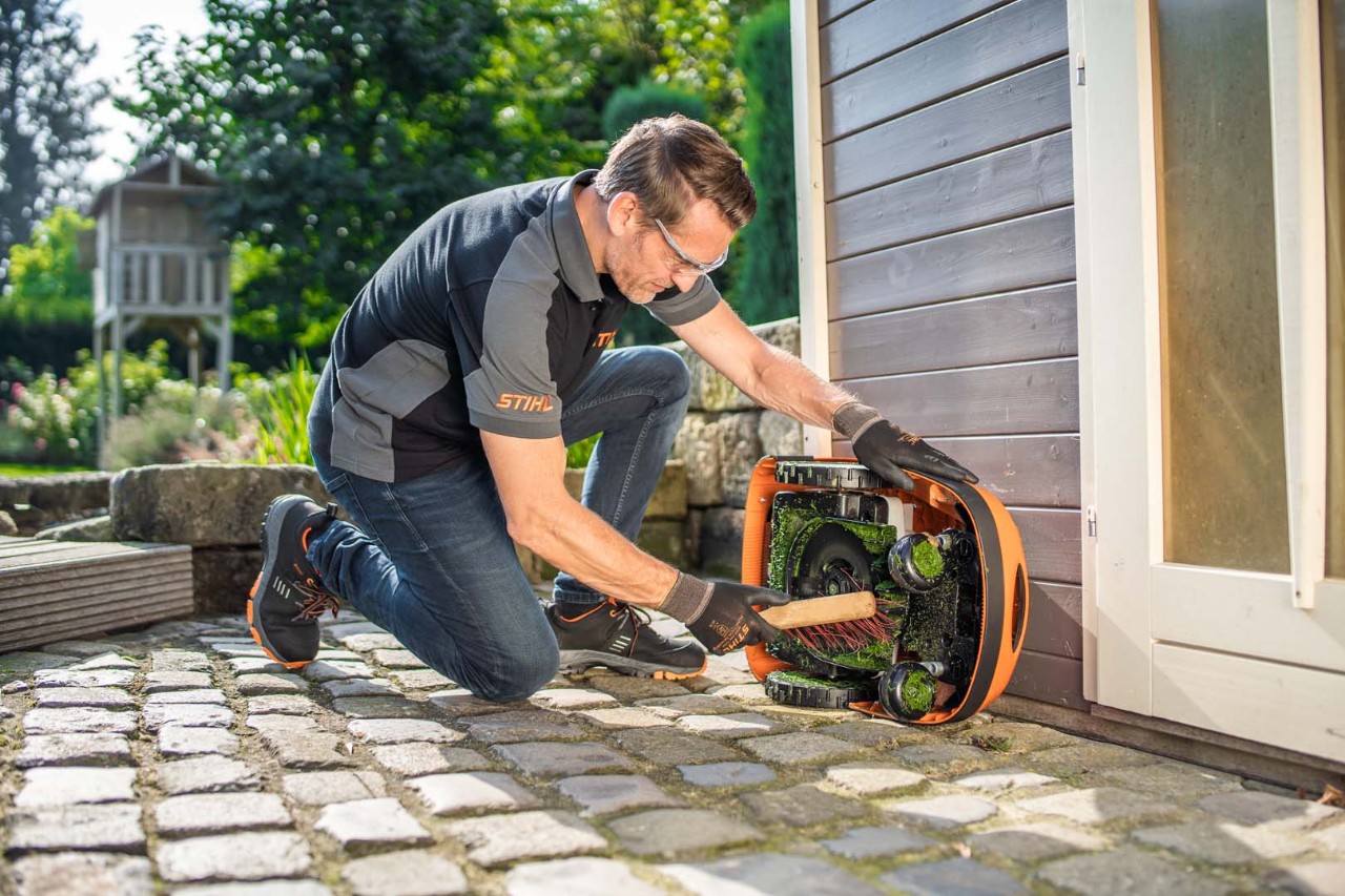 Mies puhdistamassa harjalla STIHL iMOW® 422 -robottiruohonleikkurin alapuolta 