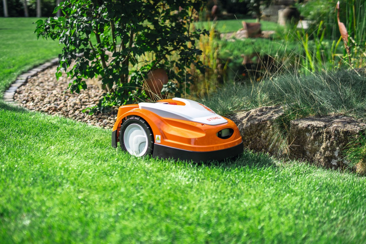 STIHL iMOW RMI 422 leikkaa nurmikkoa puutarhassa pienen kiviseinän reunalla.