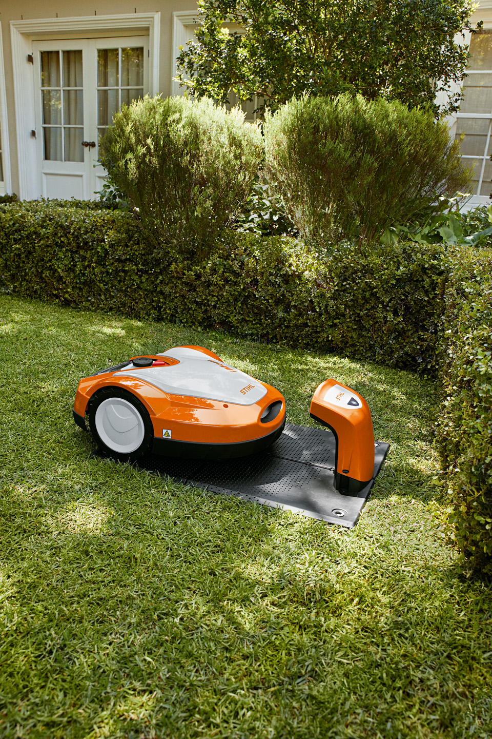STIHL iMOW® RMI 632 -robottiruohonleikkuri latausasemassa puutarhassa.