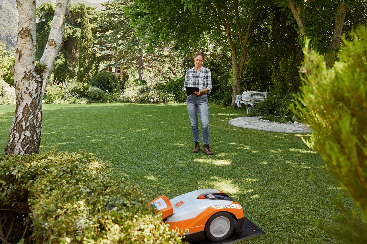 Nainen tabletin kanssa puutarhassa käyttämässä STIHL iMOW® 522 -robottiruohonleikkuria