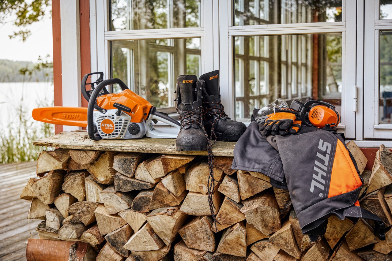 STIHL-suojavaatteet ja MS 162 hyllyllä polttopuupinon yläpuolella