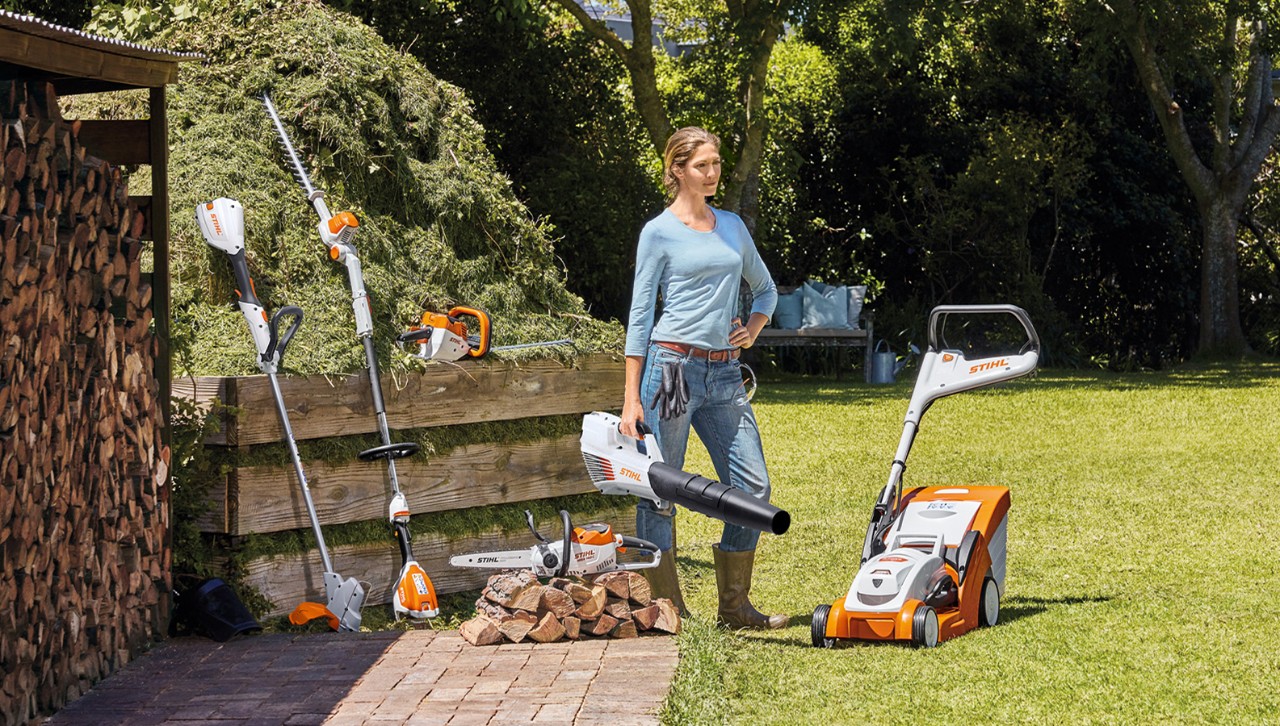 Nainen seisoo puutarhassa STIHL-akkutuotteiden kanssa
